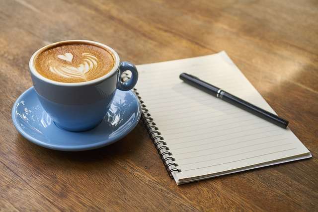 Nur noch schnell ein Kaffee, dann lege ich los... Notizbuch mit Stift und Kaffeetasse mit Herz im Milchschaum